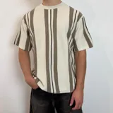 Remera de punto color crema con rayas verticales marrones y negras, de corte holgado y mangas cortas.