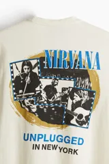 Remera color crema de corte holgado con cuello redondo y estampado frontal con el logo de la banda Nirvana y la frase 'Unplugged in New York' en color azul.