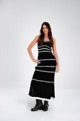 Vestido largo de punto calado blanco con rayas horizontales negras y breteles finos. El vestido tiene un corte recto y aberturas laterales en el ruedo. Las modelos llevan sombrero de estilo cowboy y botas de cuero.