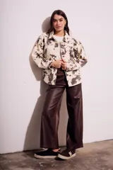 Campera de algodón color crema con estampado de manchas marrones tipo vaca, corte al cuerpo, con cuello clásico, cierre frontal con botones y bolsillos de parche en el pecho.