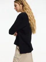 Cardigan negro de tejido con botones en la parte delantera y tajos verticales laterales.