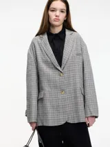 Blazer gris a cuadros con solapas de muesca, cierre con dos botones y corte holgado. Incluye un prendedor de flor negra en la solapa.