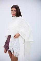 Poncho blanco de tejido calado con diseño geométrico y flecos en el borde.