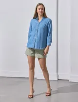 Camisa celeste de tencel con cuello con solapa, escote en V, abertura central con botones, bolsillo aplicado en el frente y ruedo desflecado.