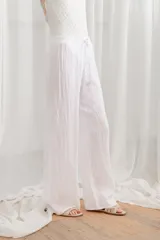 Pantalón de lino blanco, de corte ancho y tiro alto, con cintura elastizada y cordón ajustable.