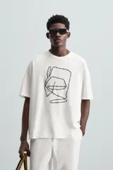 Camiseta blanca de corte relaxed fit, cuello redondo y manga corta. Presenta un bordado abstracto en color negro en el frente.