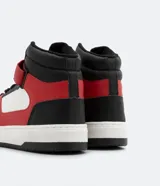Championes de caña alta, color blanco, rojo y negro, con ajuste de cordones y velcro. Suela bicolor y puntera redondeada.