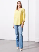 Blusa blanca de tejido labrado con cuello redondo, escote en V y aplique metálico.