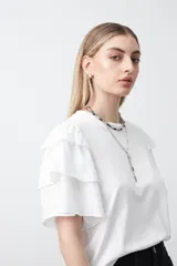 Remera blanca de algodón con mangas cortas compuestas por volados en capas, lo que le da volumen y movimiento.