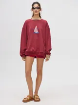 Buzo blanco de corte redondo (crew neck) con puños ajustados que tienen rayas rojas y blancas. Presenta un estampado central de un velero navegando con texto alrededor.