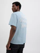Camiseta celeste de manga corta y cuello redondo con estampado en el frente que dice 'Studio Originals Edition'.
