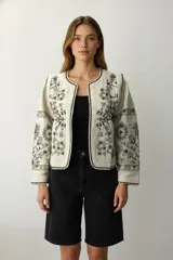 Chaqueta corta color crudo con bordados florales negros, cuello redondo y corte holgado.