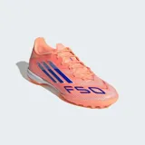 Championes de fútbol Adidas F50 League para pasto artificial, color naranja con tres franjas azules en el lateral y la inscripción "F50" en la puntera. Cuentan con mediasuela de EVA y suela de caucho con tacos bajos.