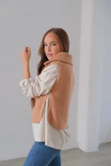 Chaleco de punto color camel, con cuello alto, medio cierre frontal y botones decorativos en los laterales.