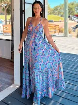 Vestido largo tipo solera, con escote en V y tirantes finos, confeccionado en seda estampada con motivos florales y patrones geométricos en tonos azules, naranjas y morados. Presenta un corte amplio y volados en el ruedo.