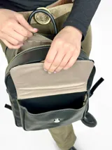 Mochila grande de cuero negro con bolsillo frontal de charol y cierre superior.