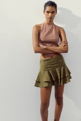 Falda pantalón corta color verde oliva, de tiro medio con detalle de pliegues en la cintura y volantes en el ruedo.
