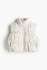 Chaleco puffer color crema con cuello alto, cierre frontal y bolsillos laterales invisibles.