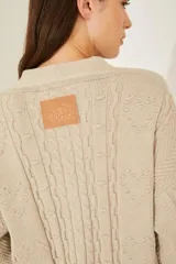 Cardigan tejido color beige con cuello en V, cierre con botones, mangas largas con puños acanalados y bordados con motivos florales.