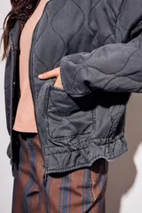 Campera acolchada gris oscuro con efecto lavado, cuello mao y cierre frontal. Presenta un patrón de costura ondulado.