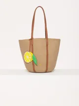 Bolso tote de hilo color beige con estructura firme y diseño espacioso. Tiene correas largas de cuero vacuno color marrón para llevar al hombro, aplique frontal de limón y logo metálico JCH.