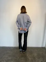 Camisa a rayas verticales azules y blancas, de popelina de algodón, con cuello verde y botones marmolados. Es corta adelante y larga atrás.