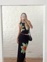 Conjunto de dos piezas negro, compuesto por un top sin mangas ajustado y una falda larga y fluida. Ambas prendas tienen un estampado grande y difuminado de una flor en tonos verde claro y rojo anaranjado.