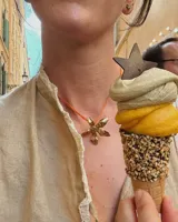 Collar con cordón naranja y dije de flor dorada.