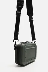 Bandolera rígida negra con formato de caja. Tiene un compartimento principal con cierre de cremallera, un bolsillo interior plano y asa de hombro ajustable y extraíble.