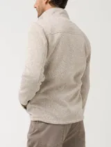 Campera polar color beige jaspeado, con cuello alto, cierre frontal completo y bolsillo vertical con cierre en el pecho.