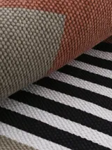 Alfombra rectangular de algodón color blanco con franjas horizontales negras y detalles en color ladrillo. Incluye flecos en los extremos.
