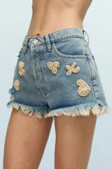 Short de jean celeste con bordados de canutillos y lentejuelas beige con formas asimétricas. Tiene roturas y terminación desflecada.