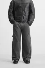 Pantalón gris oscuro de corte amplio, con bolsillos frontales y traseros de parche. Incluye un bolsillo lateral con cierre de cremallera.