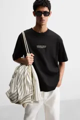 Camiseta negra de corte holgado con cuello redondo y mangas cortas. Estampado frontal con la frase "Unfolding Dreams" en letras blancas.