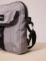 Bandolera gris de nylon con correa negra ajustable y logo Rusty estampado en negro.