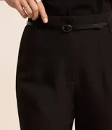 Pantalón de vestir azul marino, de corte zanahoria, con cinturón fino negro con hebilla dorada.