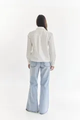 Camisa color crema con cuello clásico, cierre frontal con botones y mangas largas. Presenta detalles de bordado calado en el frente y los puños.