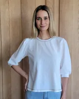 Remera blanca de algodón con mangas 3/4 abullonadas y cuello redondo. Presenta costuras a contratono en ruedo y cuello.