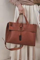 Bolso tote de cuero color marrón con correa larga ajustable y cierre con hebilla.