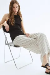 Pantalón ancho de tiro alto con elástico en la parte posterior de la cintura y cierre oculto con corchete en un lado. Bolsillos laterales discretos y piernas amplias con pliegues adelante y atrás. Diseño a rayas verticales grises y blancas.