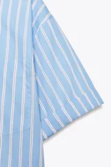 Camisa celeste con rayas verticales blancas, de corte holgado, cuello solapa, manga corta con dobladillo y bolsillo de parche en el pecho.