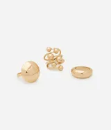 Set de tres anillos dorados de metal con diferentes diseños: uno liso y ancho, otro con una forma ovalada y otro con esferas.