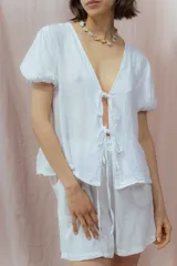Blusa blanca de lino con escote en V, mangas cortas abullonadas y cierre frontal con lazos.