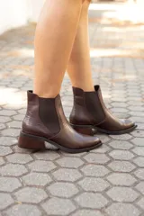 Botinetas estilo Chelsea de cuero vacuno con textura grabada tipo reptil. Presentan paneles laterales elásticos, punta almendrada y taco bajo cuadrado de madera.