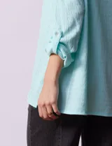 Camisa celeste texturada con cuello con solapa y abertura central con botones. Delantera con bolsillo aplicado y largo de manga regulable con presilla y botón.