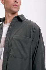Camisa de hombre color verde oscuro de pana con cuello clásico, cierre frontal con botones, dos bolsillos de parche en el pecho y mangas largas con puños abotonados.