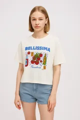 Remera color crema de algodón con estampado de tomates, botellas y la palabra "Bellissima" en azul.