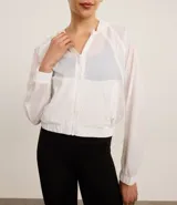 Campera rompevientos deportiva blanca, confeccionada en poliamida, con capucha, cierre delantero en cremallera, tirador gomoso y puños ajustados.
