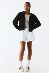 Campera con capucha negra en felpa con interior cepillado suave. Modelo con hombros caídos, capucha forrada en punto con cordón para ajustar, cierre y bolsillo canguro. Puños y bajo en punto elástico acanalado.