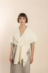 Chal asimétrico de lana color gris claro, con cortes en los hombros y doble ojal de fieltro para mantener el cruce. Terminación pespunteada y al corte.